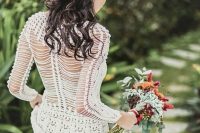 a crochet A-line wedding dress with an illusion back and long sleeves, a bold floral hairpiece and a bouquet for a boho summer or fall bride