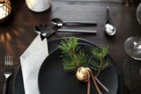 a dark Christmas tablescape with black plates, evergreens, bells, printed napkins, candles and bulbs
