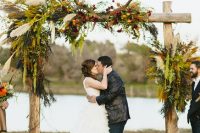 a fall wedding arch decorated with greenery, pampas grass, berries, bright blooms and antlers is a beautiful decoration