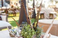 a fall wedding centerpiece of green hydrangeas, thistles, feathers, antlers and candles in glasses wrapped with birch bark