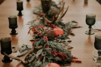 a fall wedding tablescape done with a greenery, red bloom adn berry runner, moss, artichokes, pomegranates and antlers is fantastic