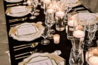 a glam black and white NYE wedding table setting with a black tablecloth, white plates and chargers, floating candles and silver cutlery