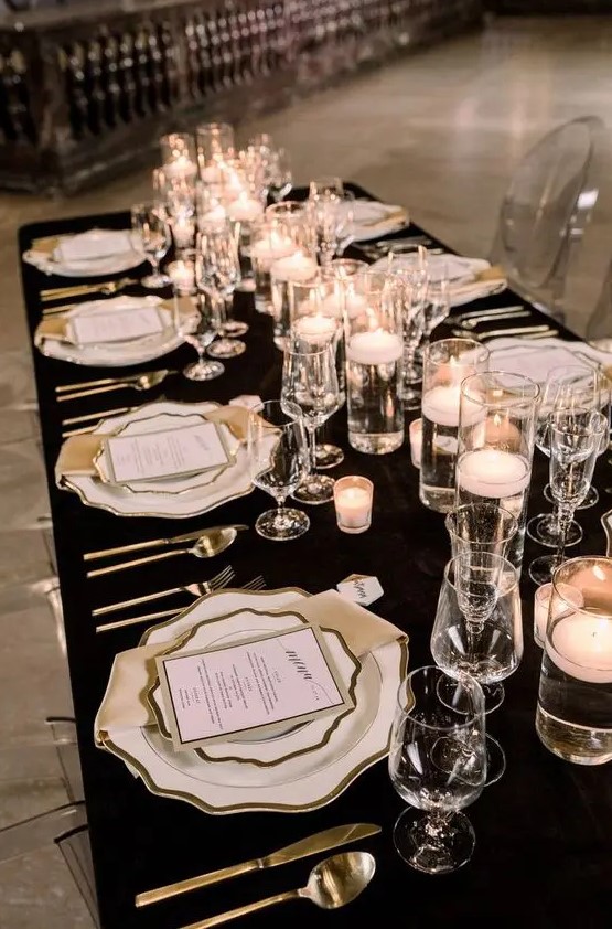 a glam black and white NYE wedding table setting with a black tablecloth, white plates and chargers, floating candles and silver cutlery
