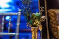 a gold glitter vase with leaves and peacock feathers make up a bold and glam centerpiece