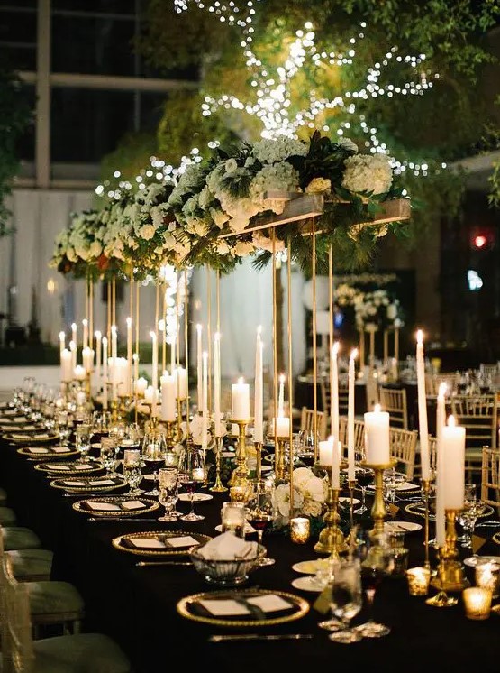 a gorgeous glam NYE wedding tablescape with pillar and thin and tall candles, a tall centerpiece with white hydrangeas and greenery