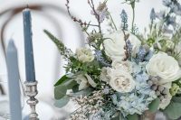 a grey and ice blue winter wedding tablescape with a floral arrangement, mercury glass candleholders is very refined and chic