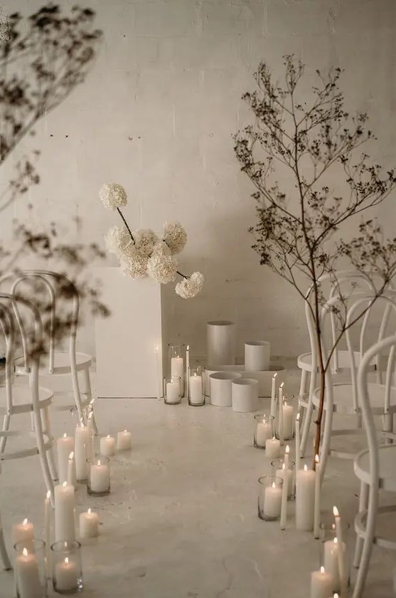 a jaw dropping minimalist winter wedding space with white blooms, vases, dried branches and pillar candles