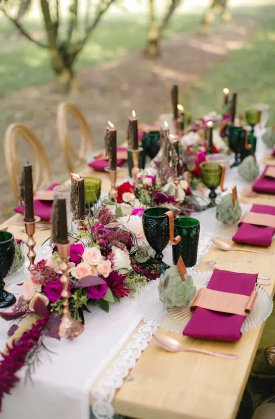 a jewel-tone wedding table setting with purple napkins and blooms, dark green candles and glasses, succulents