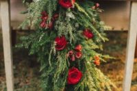 a lush evergreen table runner with red roses for a rustic holiday wedding