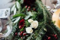 a lush greenery and evergreen table runner with white roses and berries for a Christmas wedding