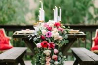 a lush greenery table garland with pink and red blooms and some candles