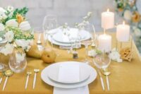 a marigold wedding tablescape with a tablecloth and matching pears, white blooms with greenery, pillar candles and gold and white cutlery