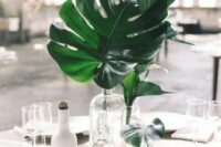 a minimalist tropical wedding centerpiece with clear glass bottles and tropical leaves