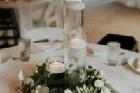 a minimalist winter wedding tablescape with a greenery and white flower wreath, candles, floating and usual ones and white linens