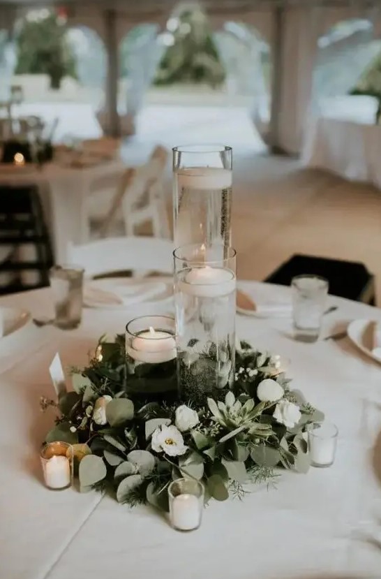 a minimalist winter wedding tablescape with a greenery and white flower wreath, candles, floating and usual ones and white linens