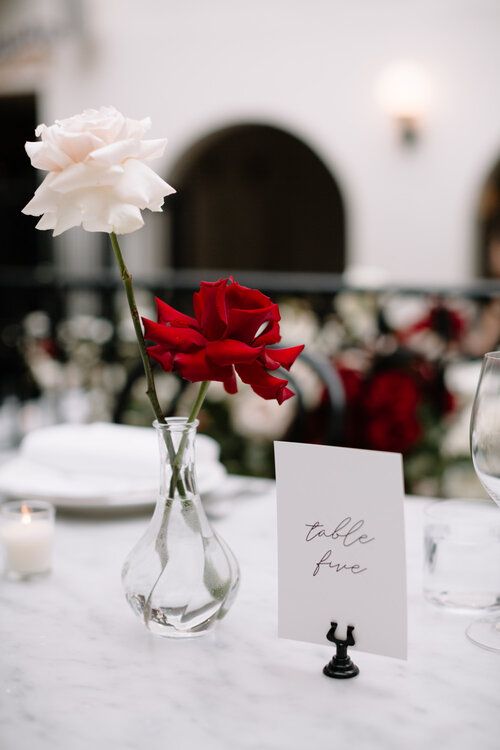 a modern and laconic wedding centerpiece of a red and a blush rose and a calligraphy table number for a classic modern wedding