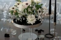 a modern black and white wedding centerpiece of a tall white stand with white roses and anemones and tall and thin candles is chic