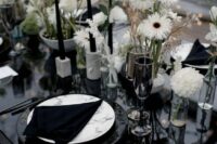 a modern cluster wedding centerpiece of lots of white blooms and leaves in various vases, tall and thin black candles in neutral candleholders