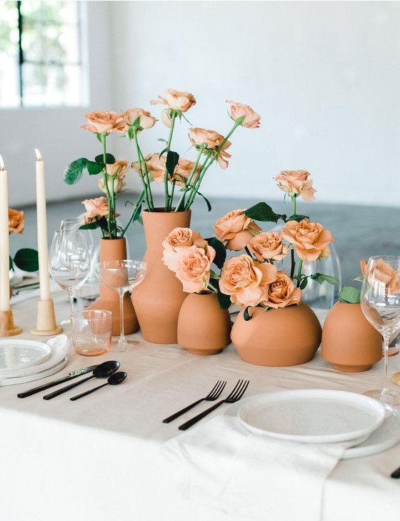 a modern cluster wedding centerpiece of terracotta vases and peachy roses looks bold and chic