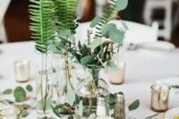 a modern cluster wedding centerpiece of vases and bottles with various greenery and candles is wow