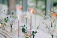 a modern cluster wedding centerpiece of white and lilac roses, tall and thin candles and smaller ones plus dried grasses