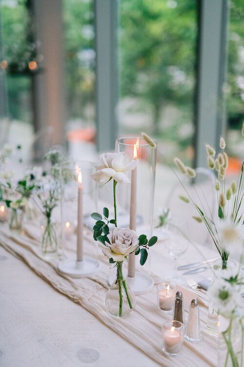 a modern cluster wedding centerpiece of white and lilac roses, tall and thin candles and smaller ones plus dried grasses