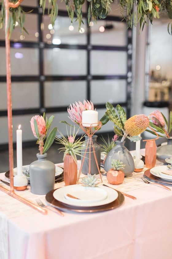 a modern cluster wedding centerpiece with copper and grey vases, bold pink blooms and greenery and candles