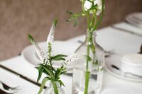 a modern laconic wedding centerpiece of clear bottles and white astilbe and ranunculus is a stylish and chic idea