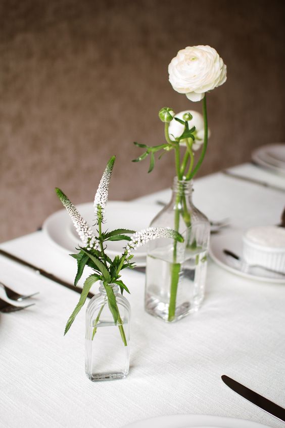 a modern laconic wedding centerpiece of clear bottles and white astilbe and ranunculus is a stylish and chic idea
