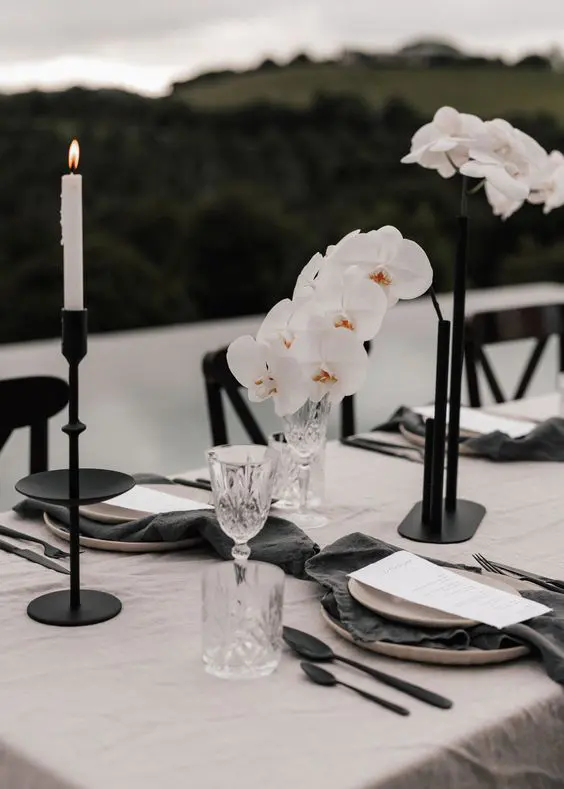 a modern refined wedding centerpiece of blakc tube vases with white orchids and white candles is a veyr stylish and chic solution