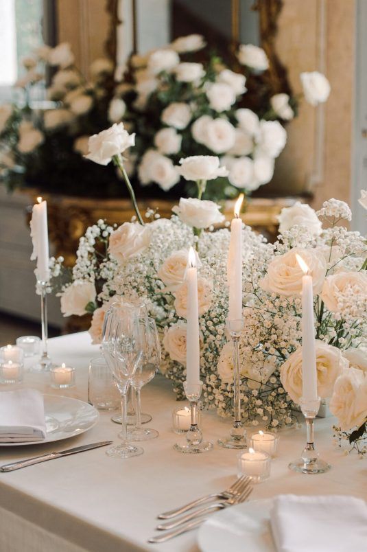 a modern romantic white wedding centerpiece of baby's breath and roses plus tall and thin and smaller candles is pure elegance and chic