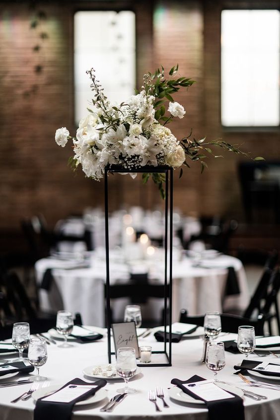 a modern tall wedding centerpiece on a black frame with white blooms and greenery is a stylish and chic idea for a modern wedding