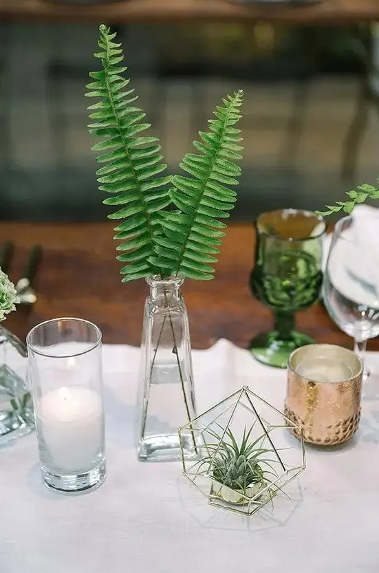 a modern urban jungle wedding centerpiece of a vase with fern leaves, succulents in a hexagon cover and candles is very cool