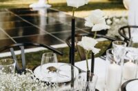 a modern wedding centerpiece of a black tube vase with white roses, baby’s breath and pillar candles is a very beautiful and contrasting idea