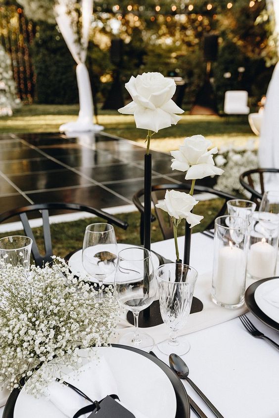 a modern wedding centerpiece of a black tube vase with white roses, baby's breath and pillar candles is a very beautiful and contrasting idea