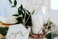 a modern wedding centerpiece of a copper lantern with candles, greenery, smaller candles, a marble table number is a lovely idea