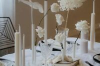 a modern white wedding centerpiece of various white blooms in various vases, tall and thin and pillar candles is pure chic