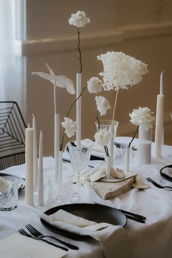 a modern white wedding centerpiece of various white blooms in various vases, tall and thin and pillar candles is pure chic