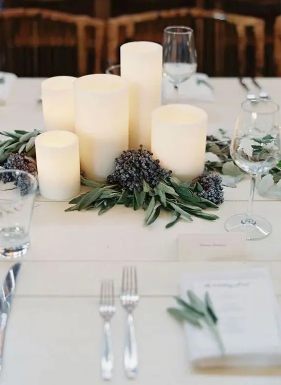 a modern winter wedding centerpiece of pillar candles, greenery and privet berries is a stylish and chic idea