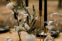 a moody cluster wedding centerpiece with sheer and white vases, black candles and white blooms, some greenery