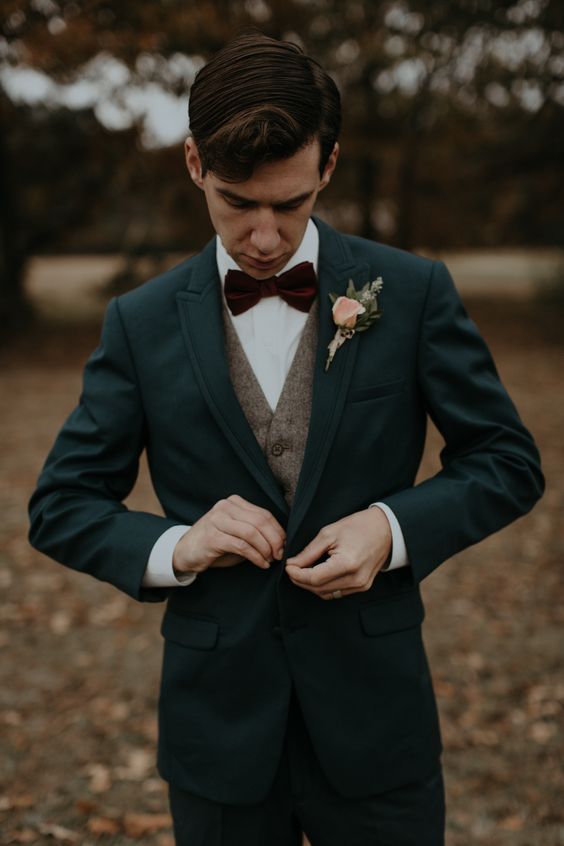 a moody winter look with a teal suit, a brown tweed waistcoat, a burgundy velvet bow tie and a floral boutonniere