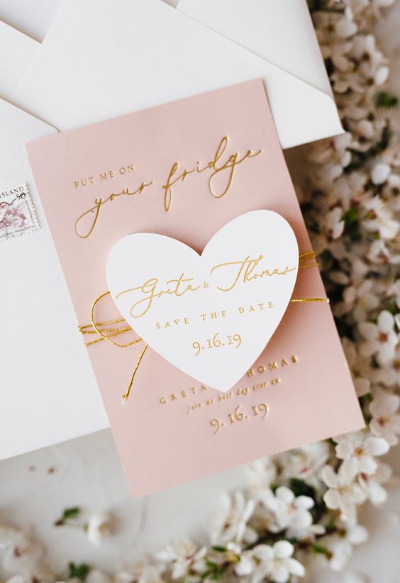 a pink and white save the date with a magnet, gold calligraphy and a wedding date is a lovely idea for a modern romantic wedding