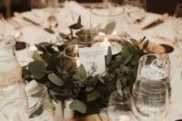a pretty and chic winter wedding tablescape in neutrals, with candles, a greenery wreath, a wooden board and some black cards