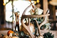 a pretty woodland wedding centerpiece of a wood slice, greenery, succulents, antlers, pumpkins and candles is amazing for a fall celebration
