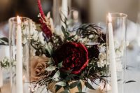 a refined Christmas wedding centerpiece of a gold bowl, greenery, burgundy and coffee roses and candles all around