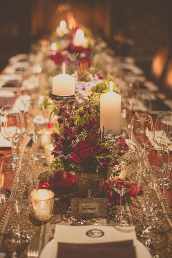 a refined Christmas wedding centerpiece of greenery, burgundy and red blooms and candles in candleholders