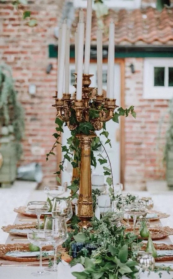 a refined and whimsy secret garden wedding tablescape with a lush greenery runner, copper chargers and tall candelabras with greenery