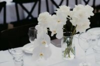 a refined modern wedding tablescape with a white tablecloth, grey and black menus, a white rose and orchid centerpiece is chic