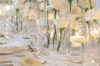 a refined white wedding tablescape with clear chargers, white roses and floating candles in glasses is a chic and stylish idea