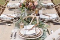 a refined woodland wedding table with a greenery runner, antlers, pastel blooms and mercury glass candleholders is very chic
